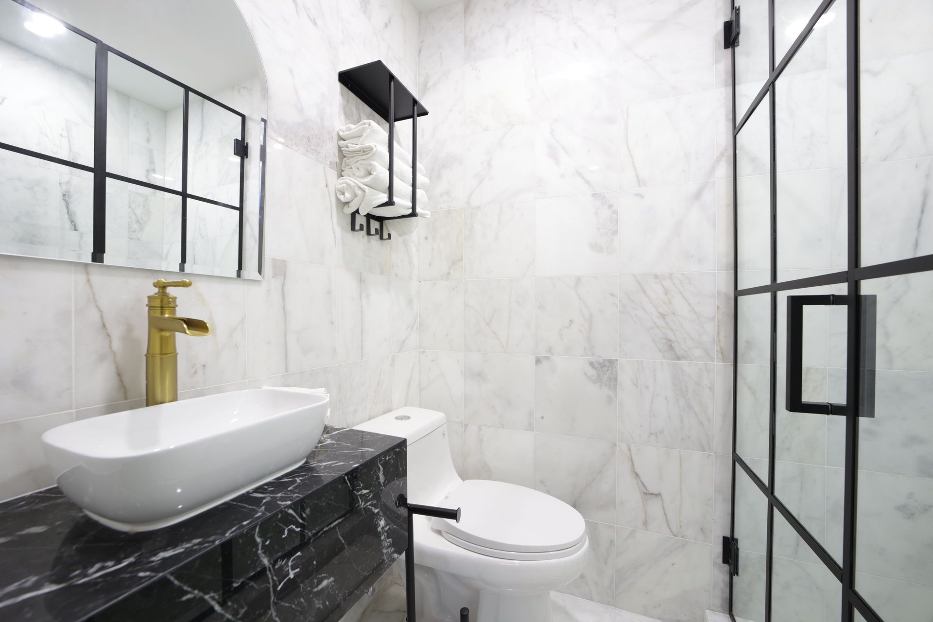 Modern bathroom with marble walls, black and gold fixtures, and a glass shower.