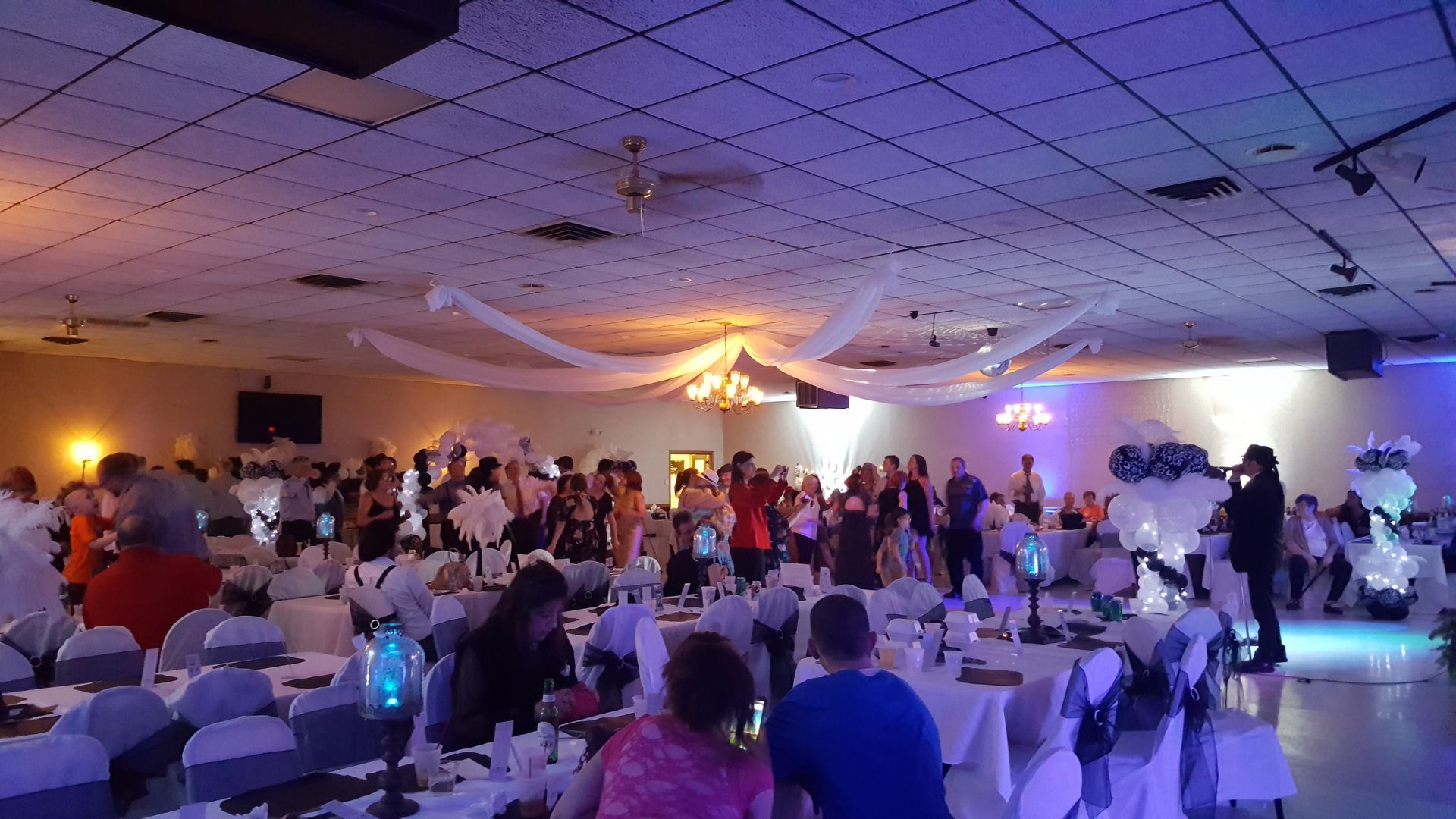 People dancing at a party under colorful lights. Back view of a woman in a red dress. Other guests are raising their arms.