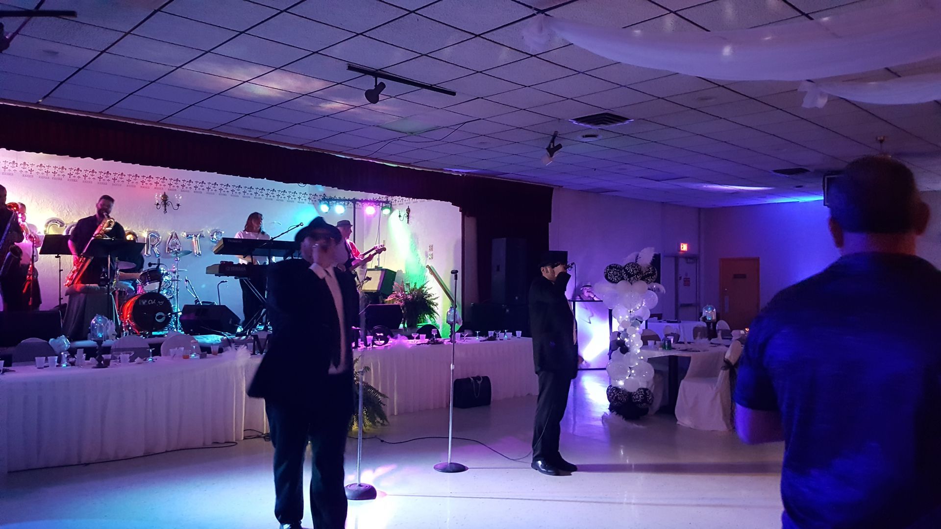 Two girls in formal dresses pose in front of a party backdrop with balloons and streamers.