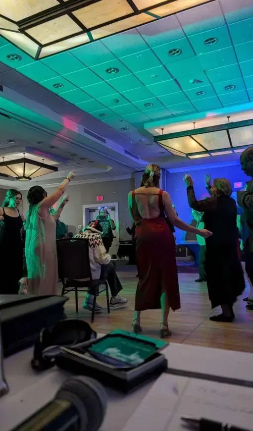 People dancing at a party under colorful lights. Back view of a woman in a red dress. Other guests are raising their arms.
