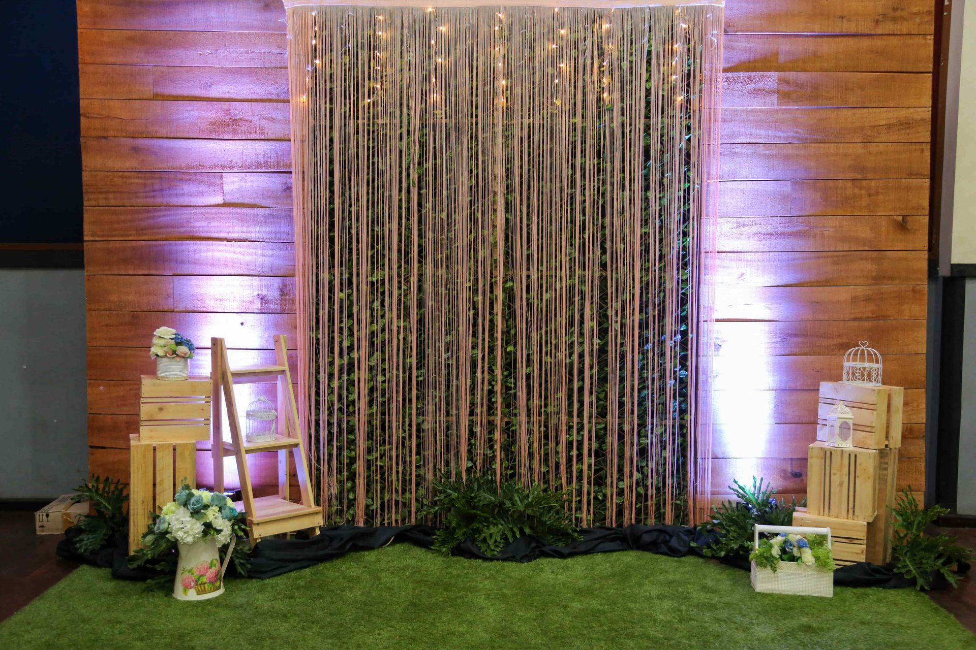 Wooden backdrop with bamboo, string lights, greenery, and wooden crates used as decor.