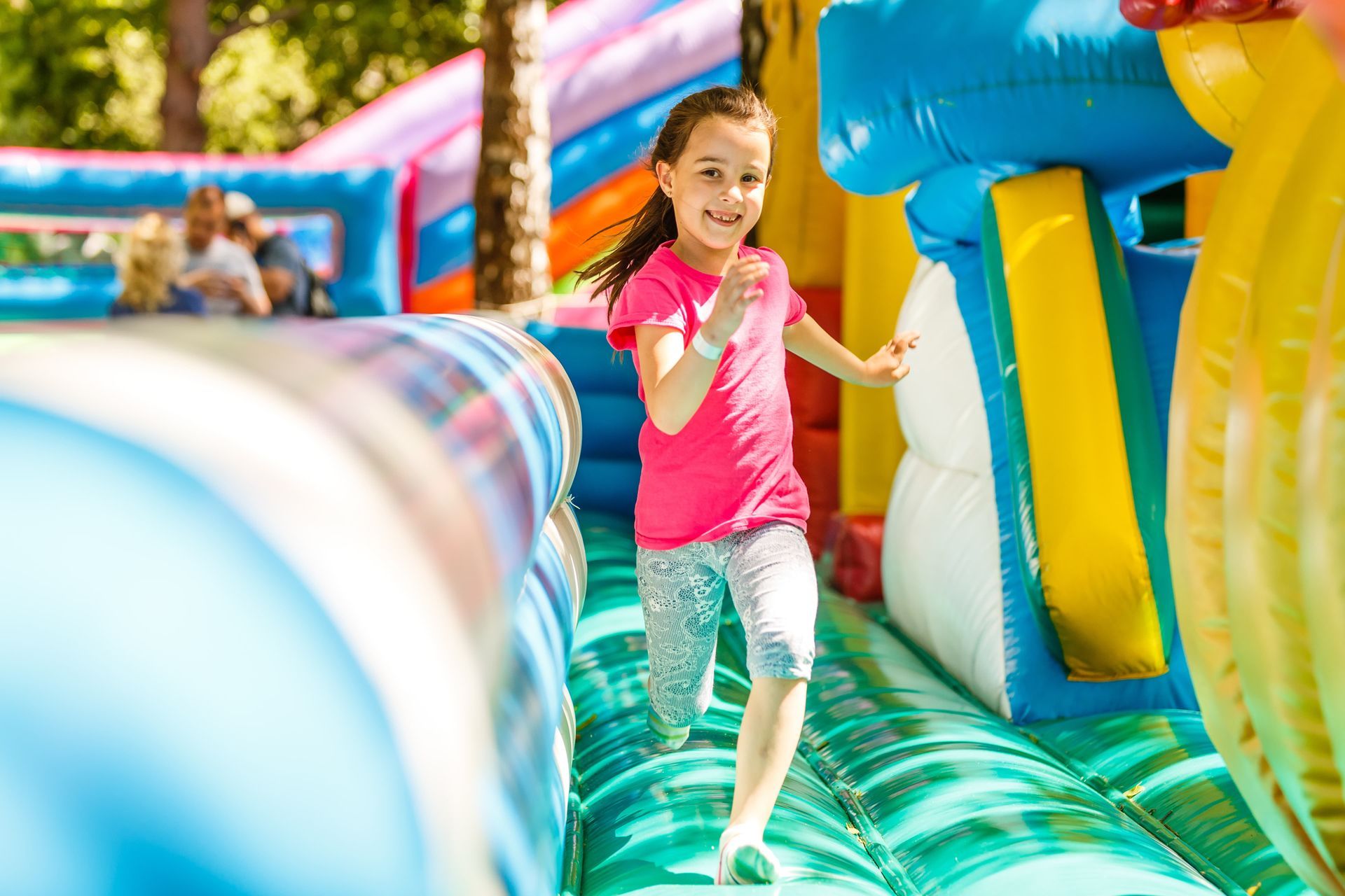 Girl in pink shirt runs through a colorful inflatable obstacle course, smiling.