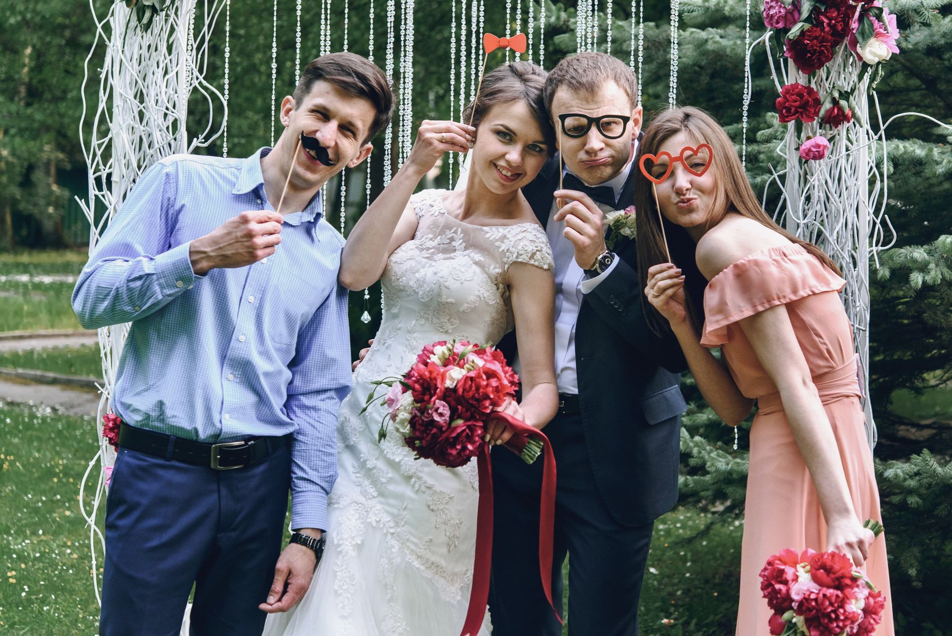 Bride and groom with two friends, posing with prop mustaches and glasses at a wedding.