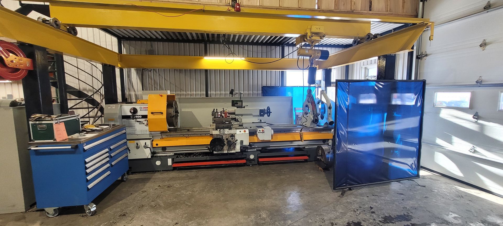 Un atelier avec une grande machine jaune et une armoire bleue sous une poutre jaune.