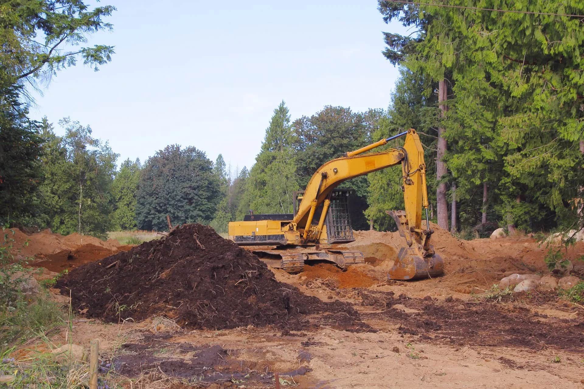A yellow excavator is working in a dirt field