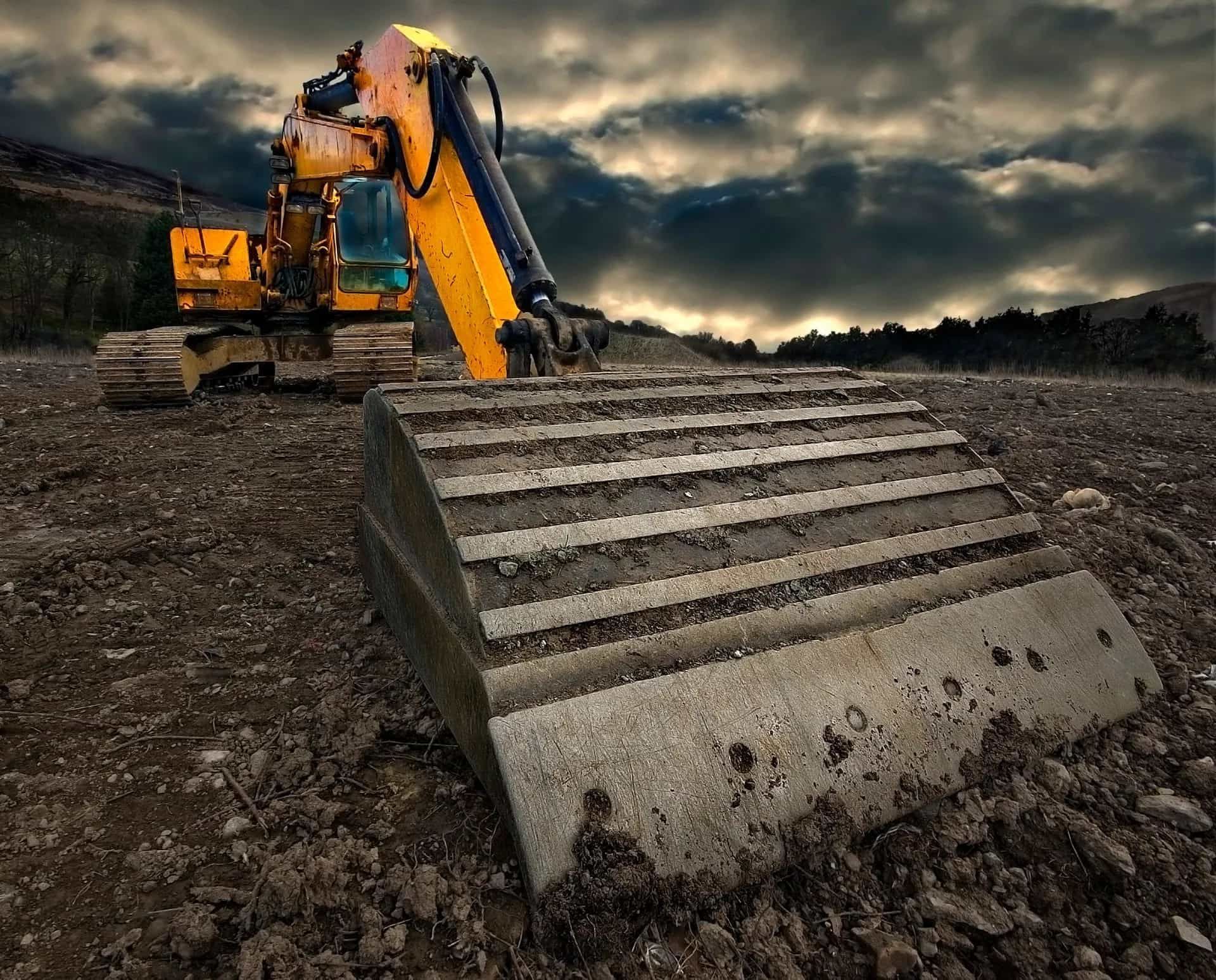 A yellow excavator is sitting on top of a dirt field.