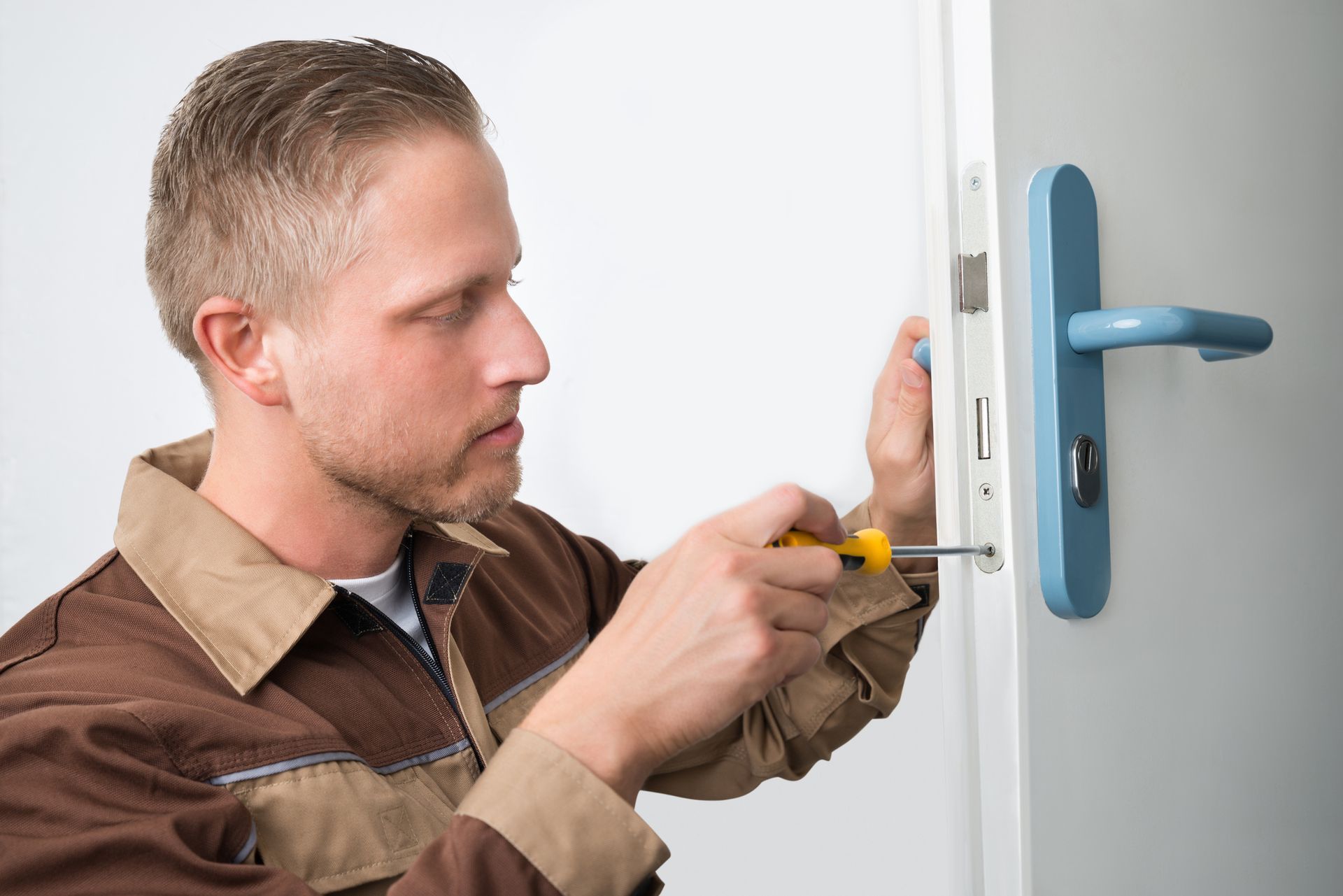 Male technician fixes white door’s lock, showcasing commercial door repair services.