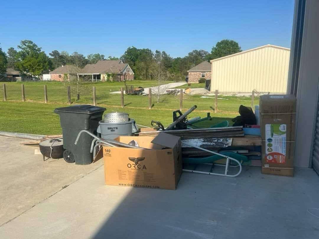 A bunch of boxes and trash cans are sitting on the sidewalk in front of a garage.