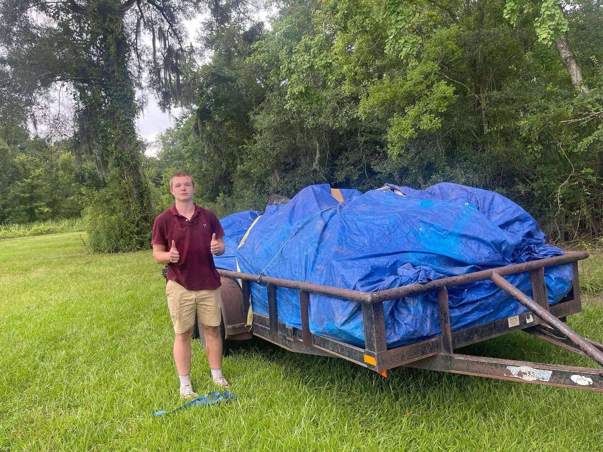 A young man is standing next to a trailer covered in blue tarps.