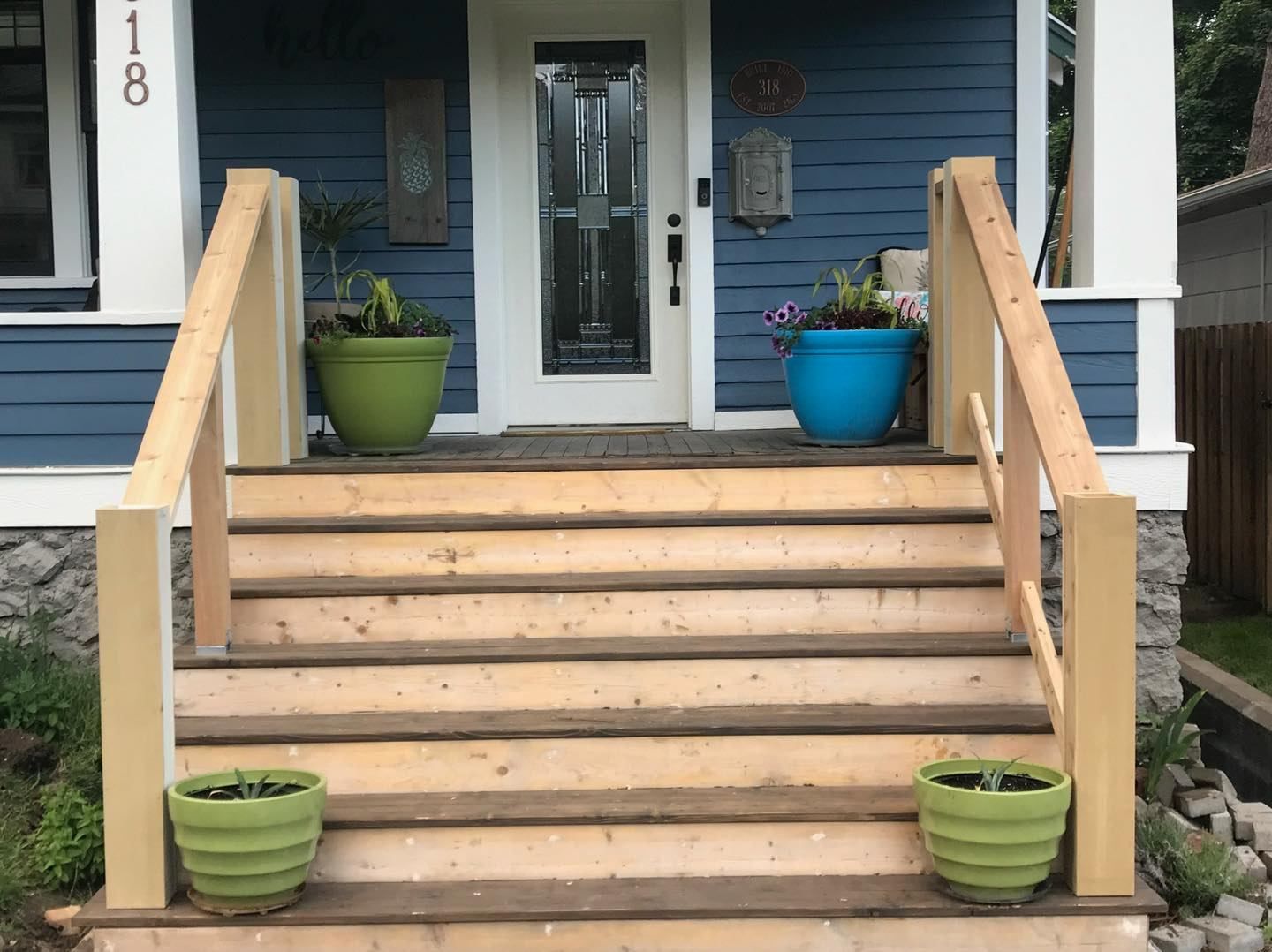 The front porch of a blue house with wooden steps and potted plants.