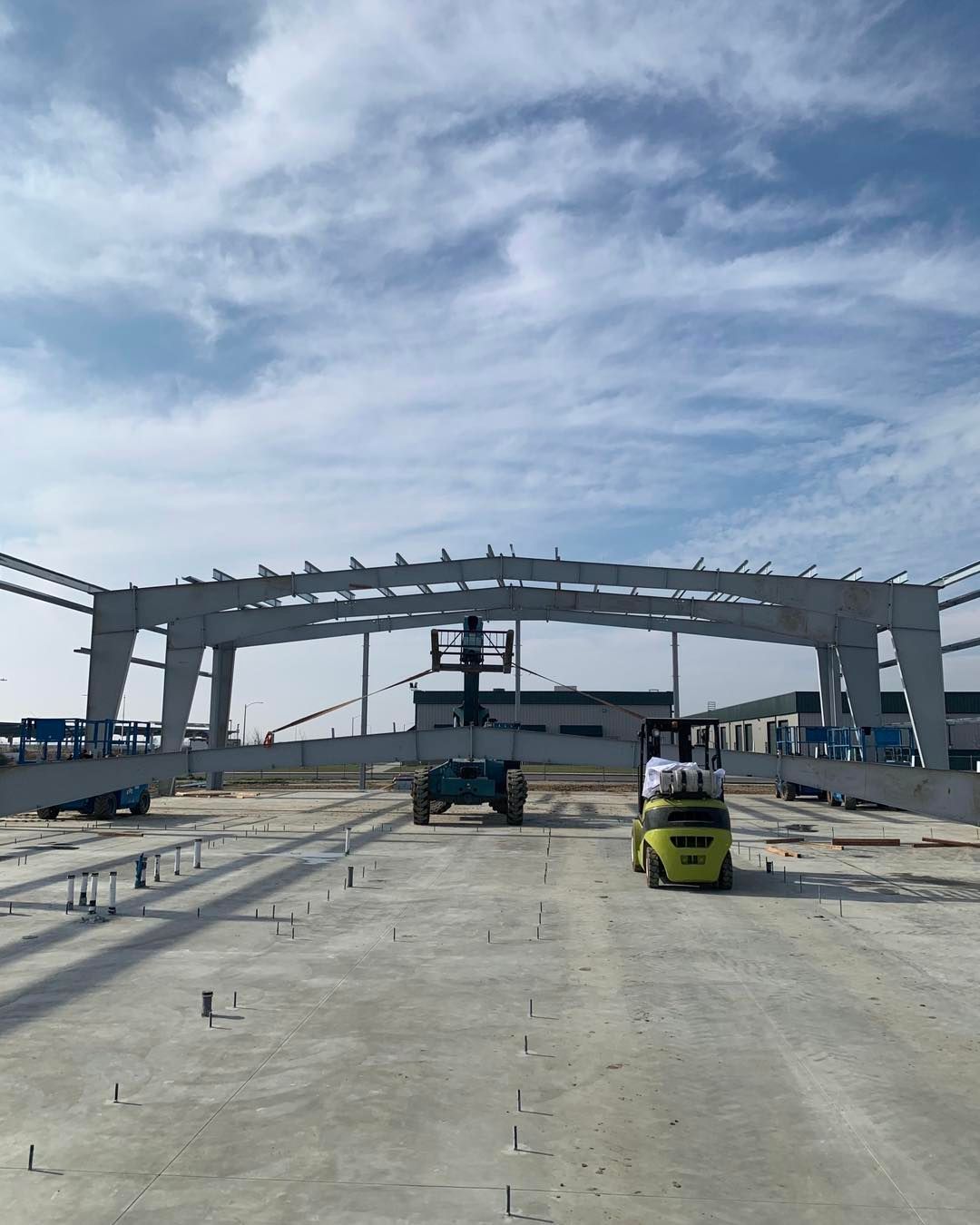 A forklift is driving in front of a large building under construction.