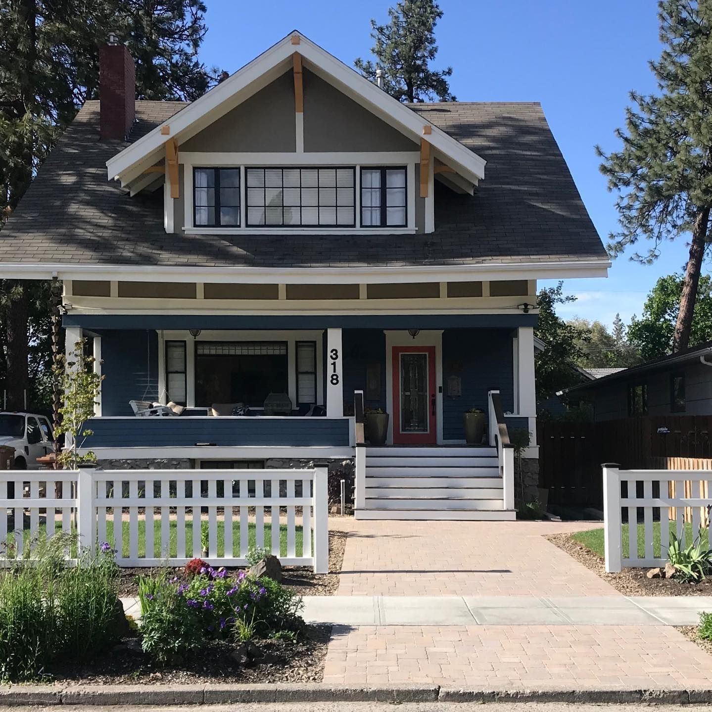 Blue craftsman-style house with white trim, front porch, and white picket fence on a sunny day