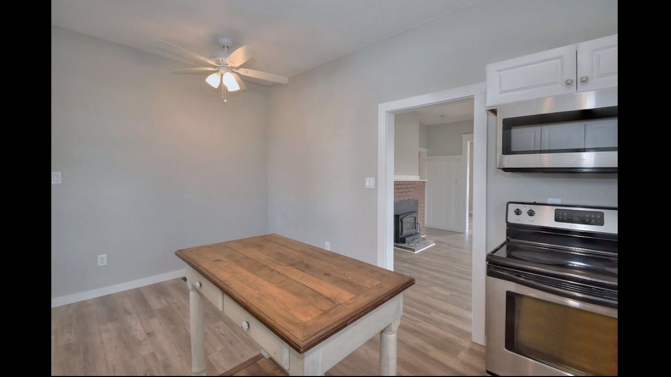 A kitchen with a table , stove , microwave and ceiling fan.