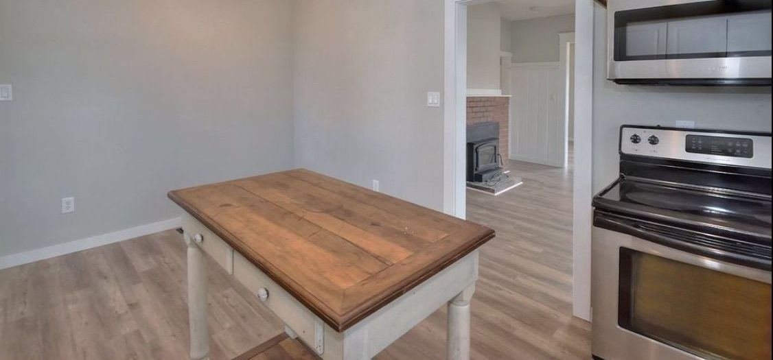 A kitchen with a table , stove , microwave and ceiling fan.