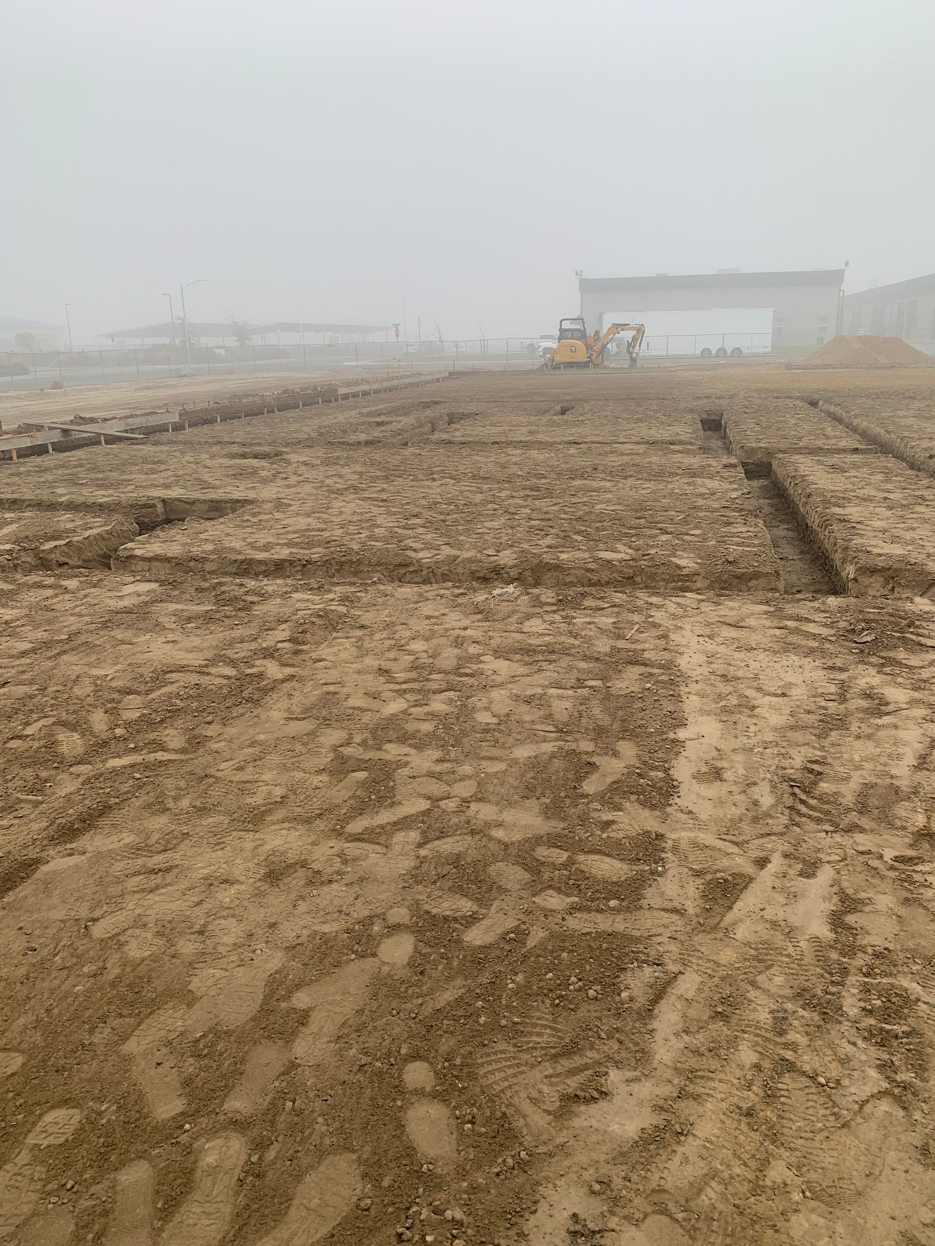 A muddy field with a bulldozer in the background on a foggy day.