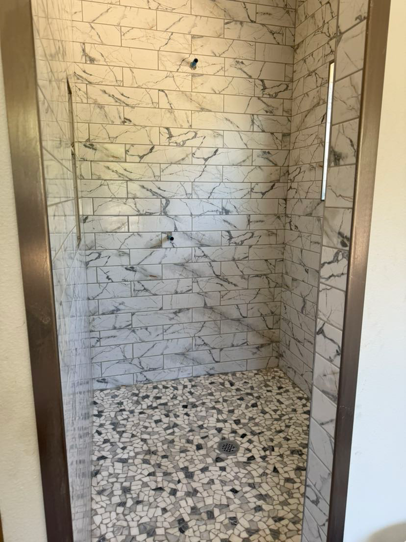 A walk in shower with marble tiles and a glass door.