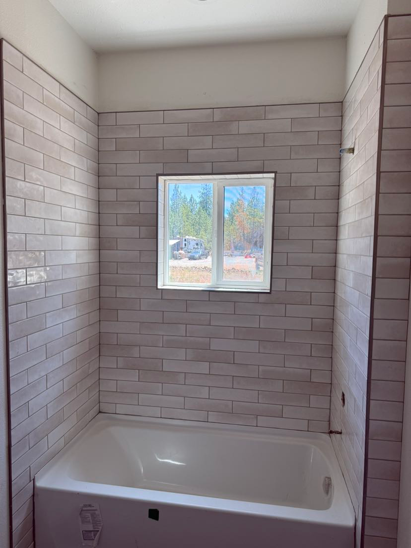 A bathtub in a bathroom with brick walls and a window.