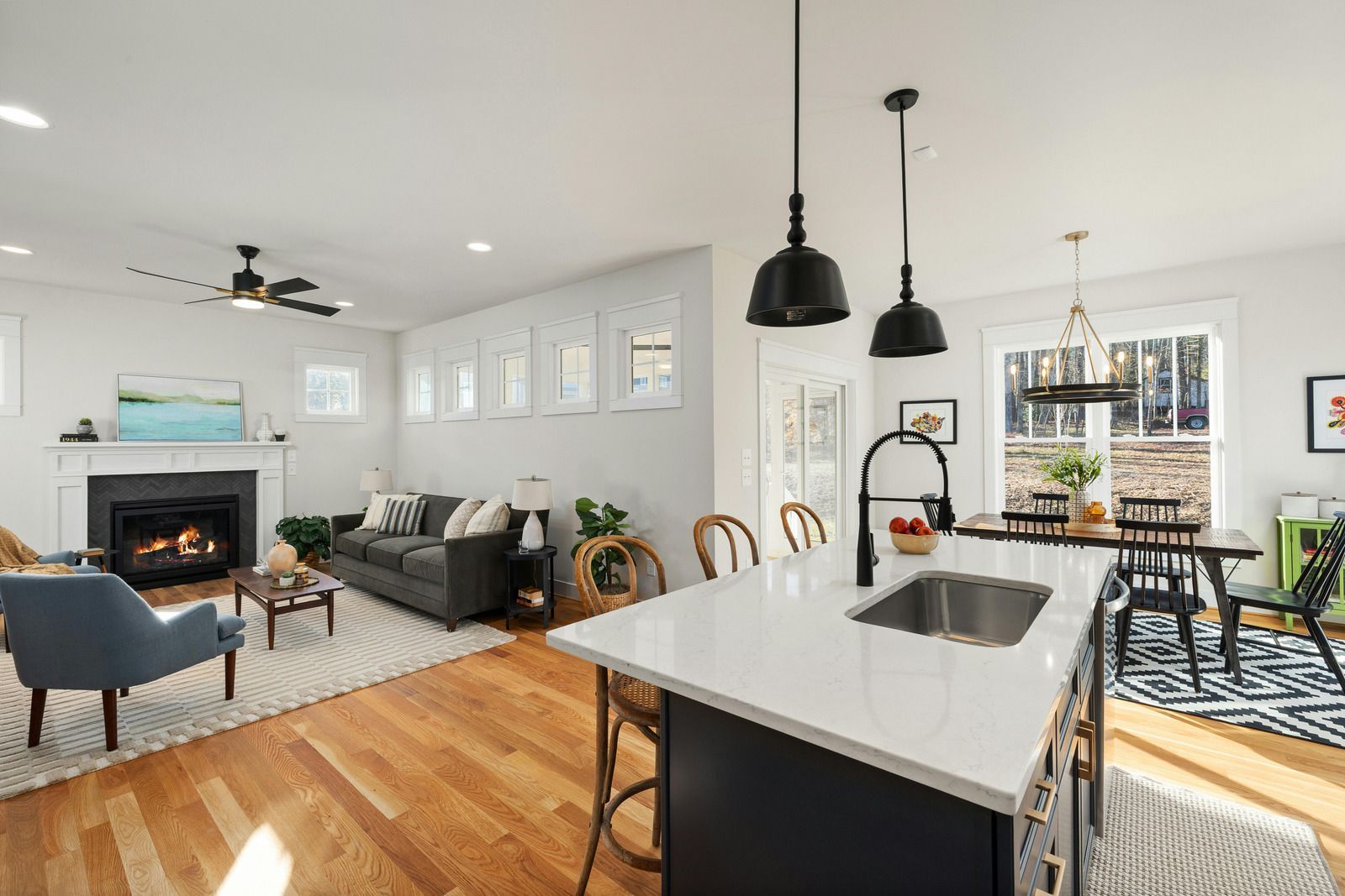Bright open-concept living room with fireplace, gray sofa, and kitchen island with pendant lights