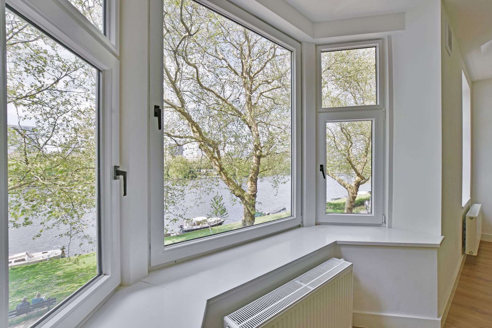 Bright white bay window nook overlooking leafy trees and water, with a radiator below.