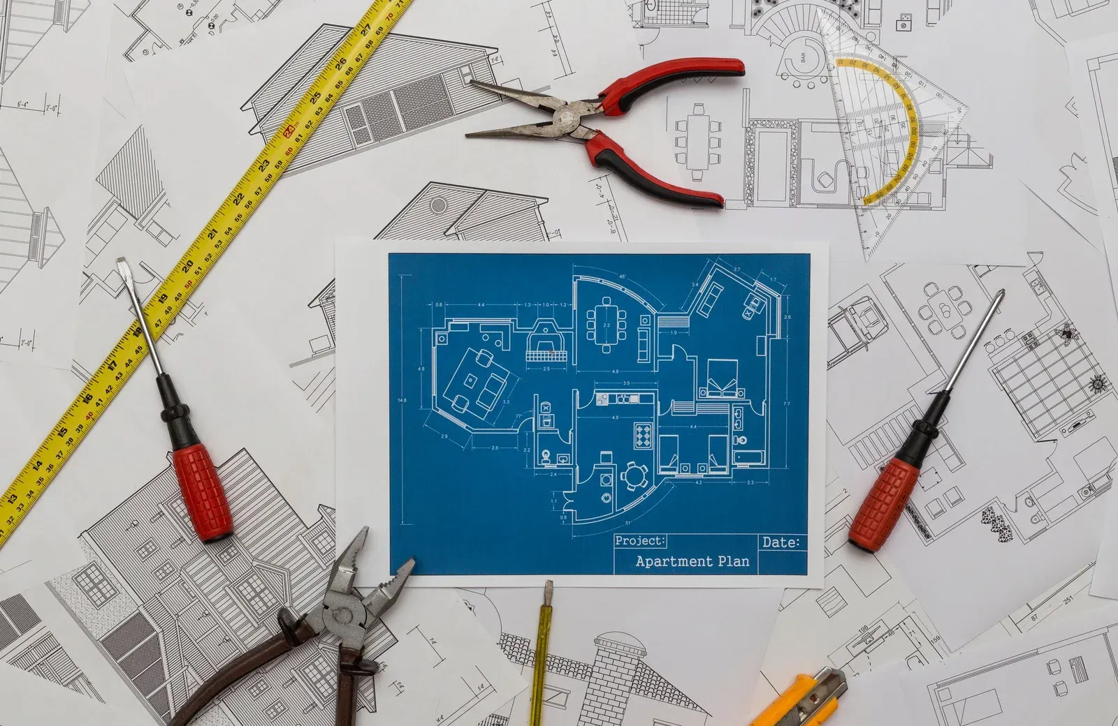 A blueprint of a house is surrounded by tools on a table.