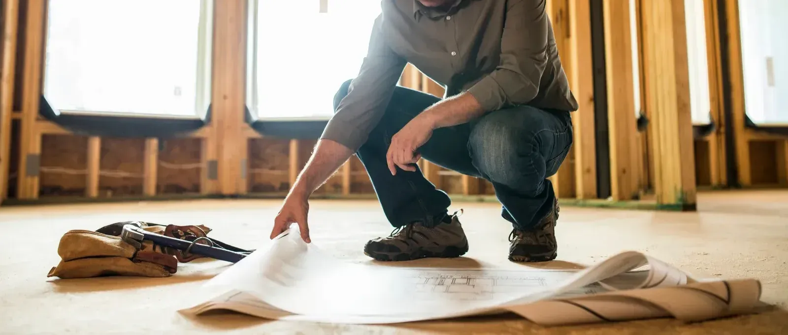 A man is kneeling down in a room looking at a blueprint.