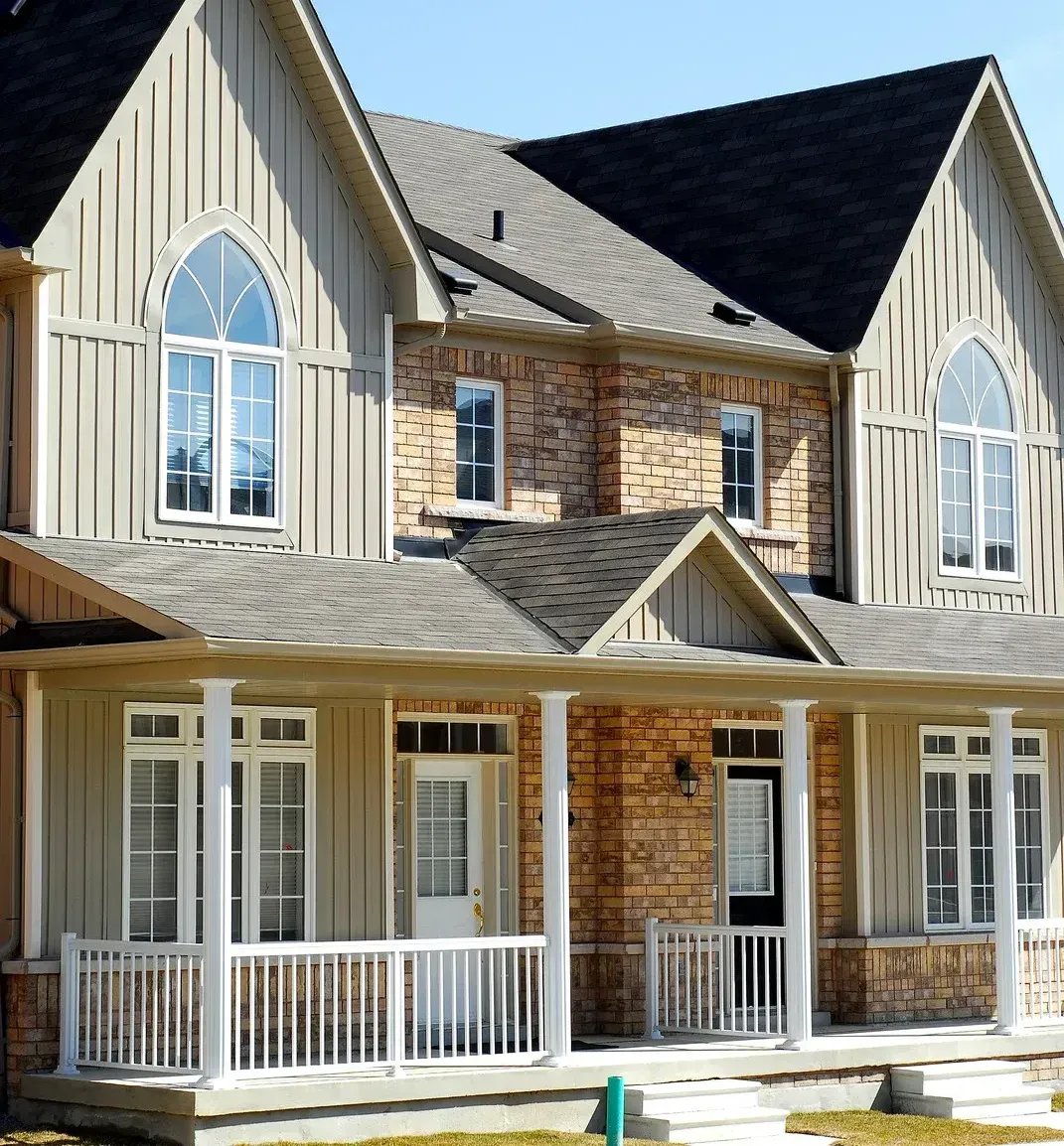 Two-story house with tan siding, brick accents, porch, and arched windows.