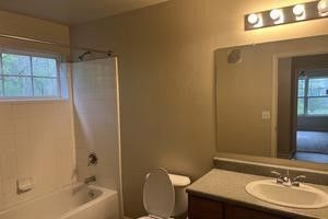 A bathroom with a toilet , sink , tub and mirror.
