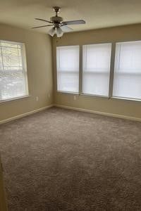 An empty bedroom with a ceiling fan and three windows.