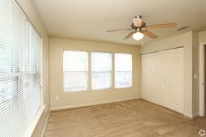 An empty room with a ceiling fan and three windows.