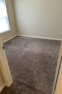An empty bedroom with a carpeted floor and a window.
