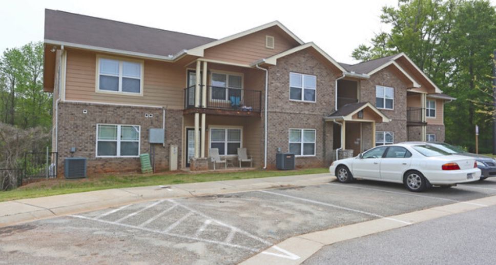 A white car is parked in front of a large apartment building.