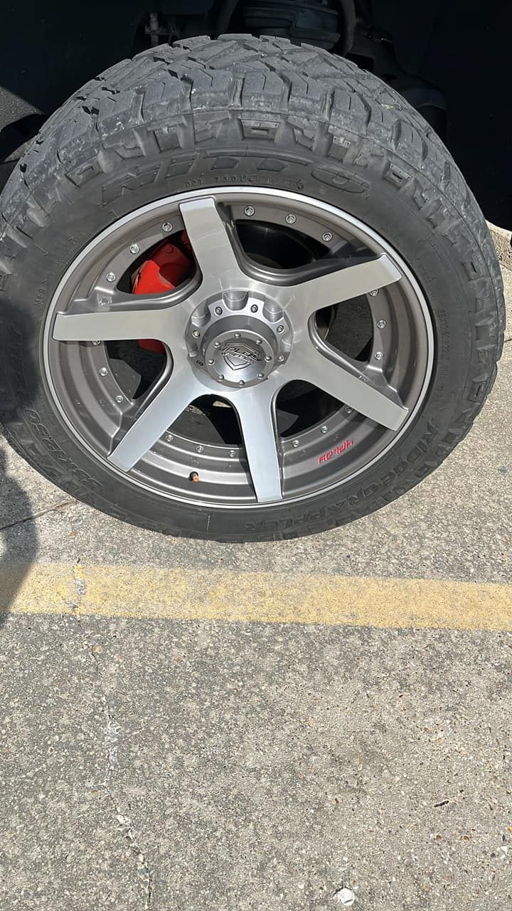 Gray and silver car tire and wheel with red brake caliper, on concrete with yellow line.