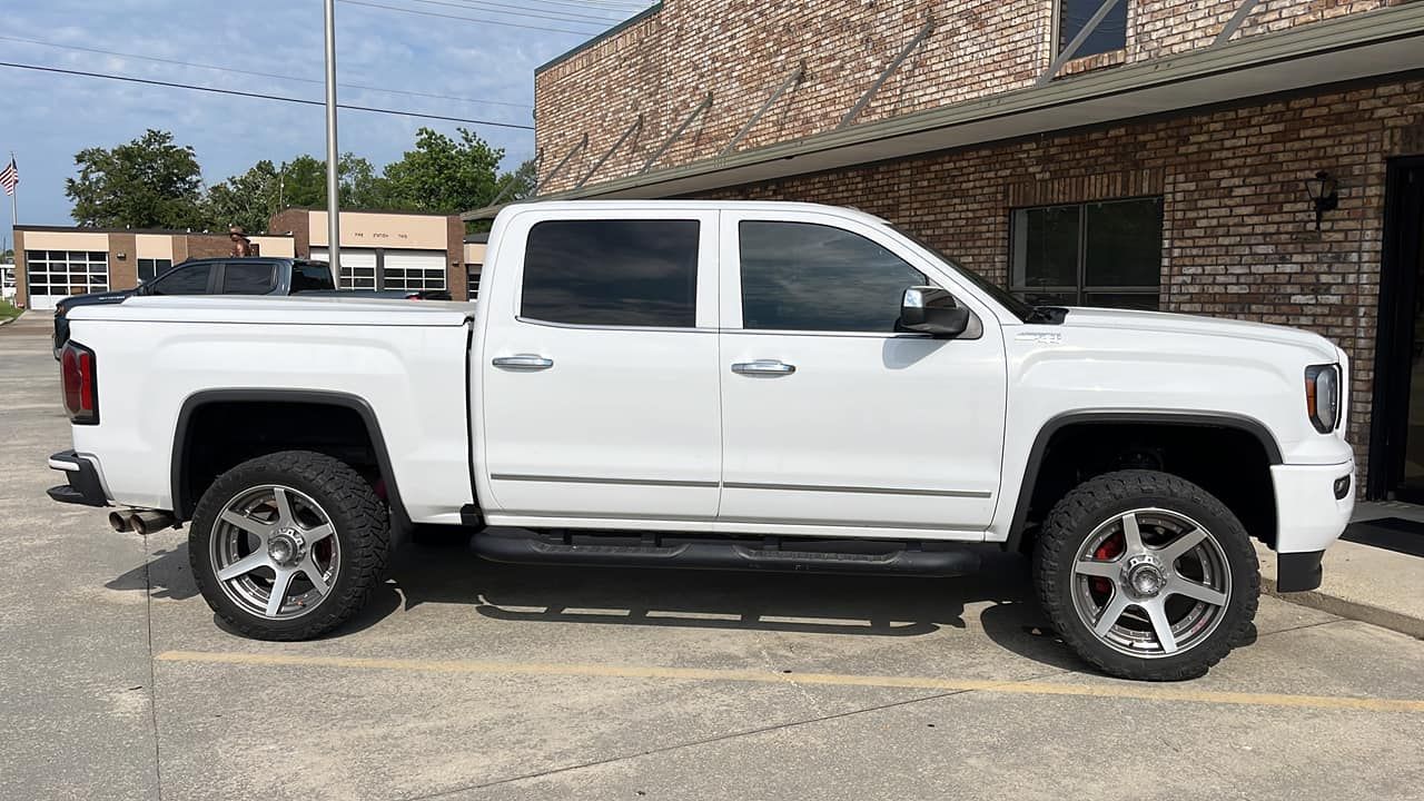 White pickup truck parked outside a brick building. Chrome wheels, tinted windows.
