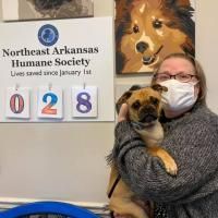 Woman holding a puppy beside a Northeast Arkansas Humane Society sign showing 028 days since Jan. 1