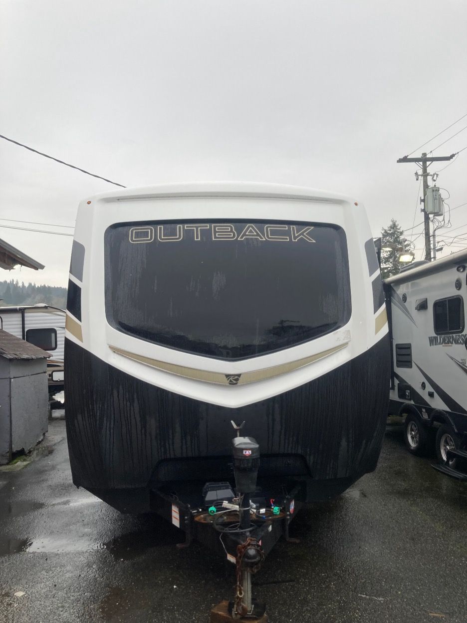 White and black Keystone Outback travel trailer. Front view in overcast conditions.