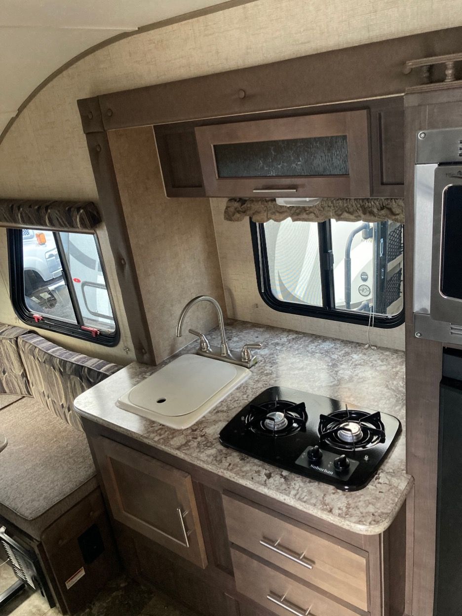 RV kitchen with stovetop, sink, microwave, and cabinets.