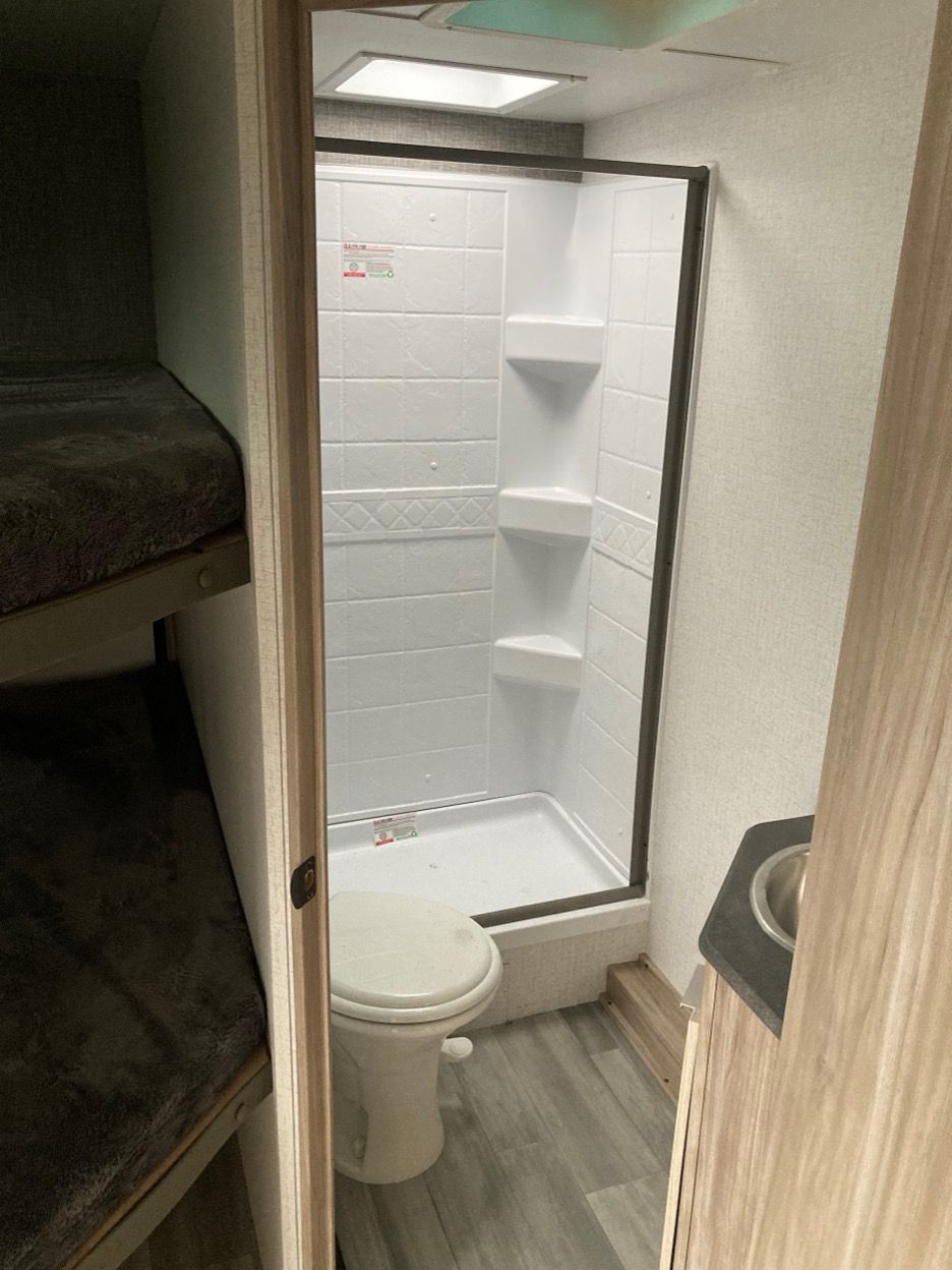 RV bathroom with toilet, shower, and bunk beds visible in the doorway.