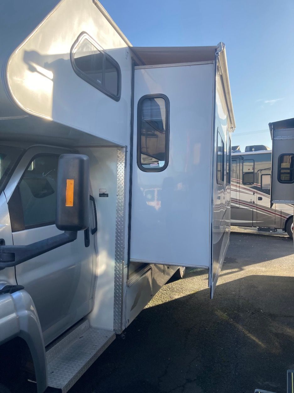 Side view of a white RV with an extended living area, parked outdoors on a sunny day.