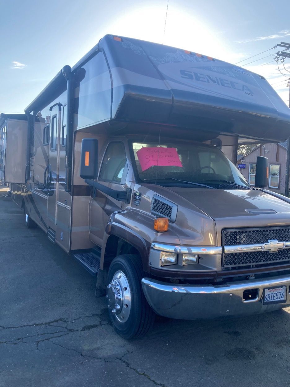 Tan and brown RV parked outdoors with a sunlit sky visible.