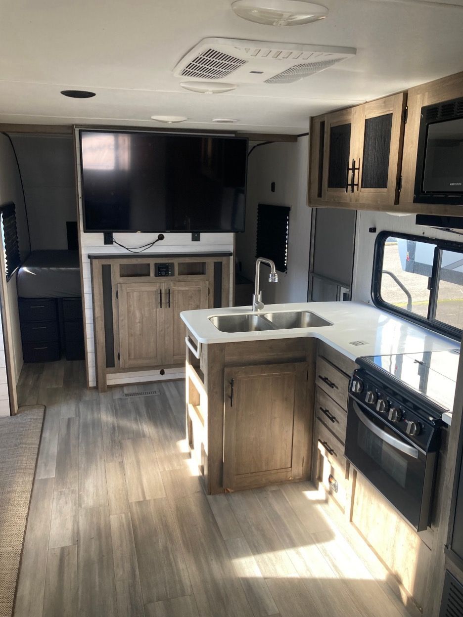 Interior view of a camper kitchen and living area with appliances and cabinets.