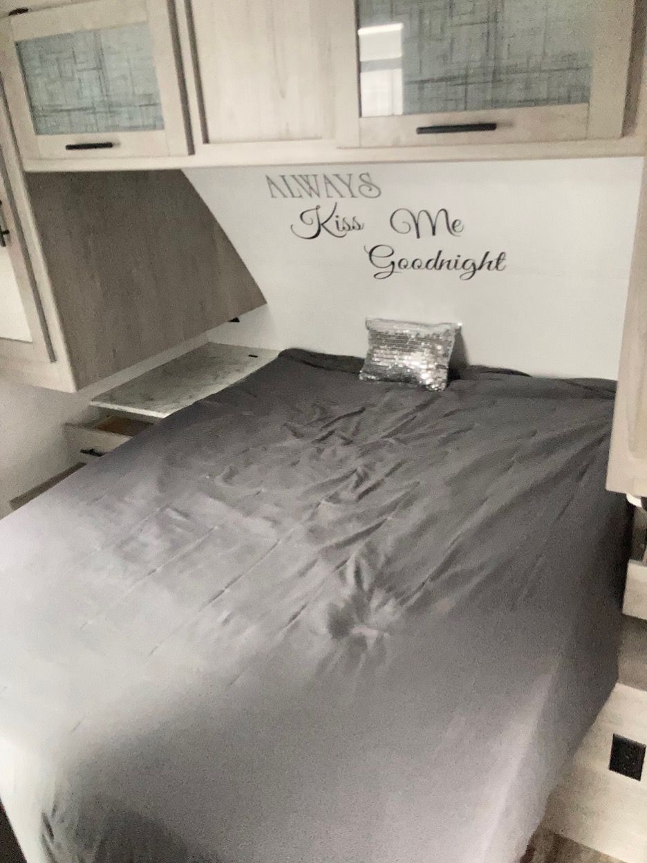 Bedroom in an RV with bed, bedding, decorative wall art "Always Kiss Me Goodnight", and storage cabinets.