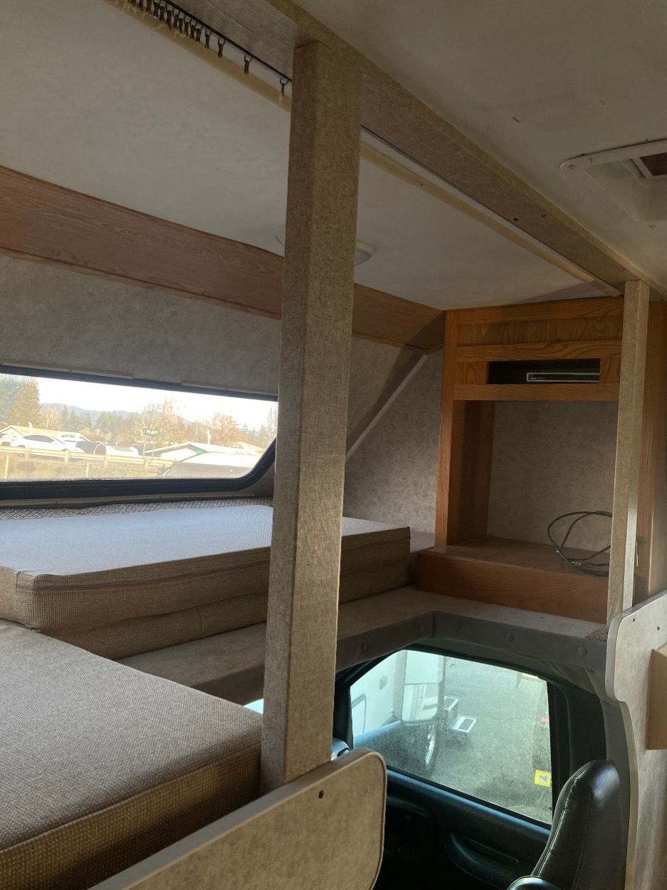 Interior of a motorhome with a loft bed above the driver's area, visible window, steps, and built-in cabinetry.