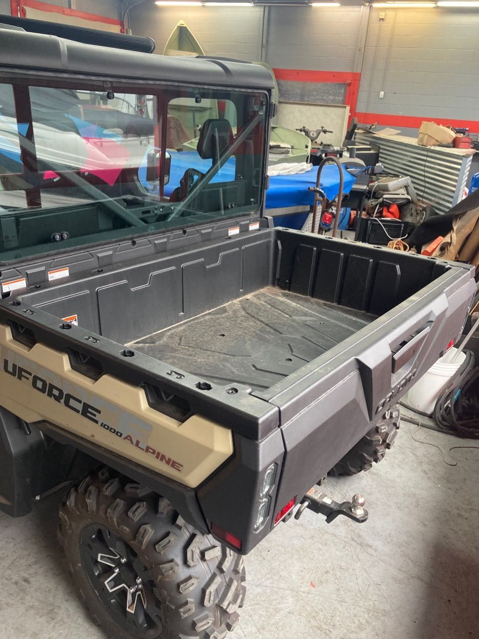 Tan and black UFORCE utility vehicle in a shop with a cargo bed and rear window.