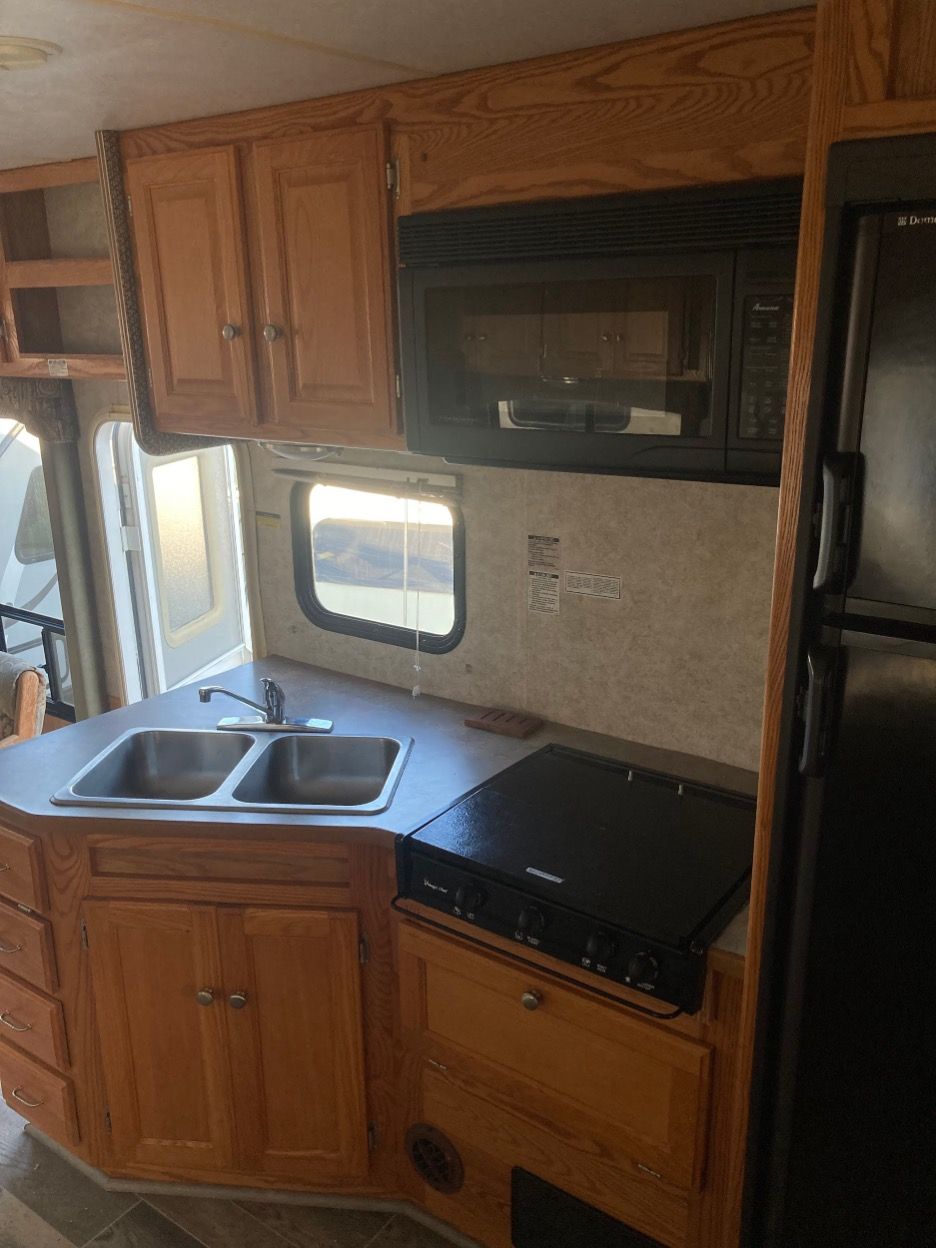 RV kitchen with wooden cabinets, sink, microwave, stove, and refrigerator.