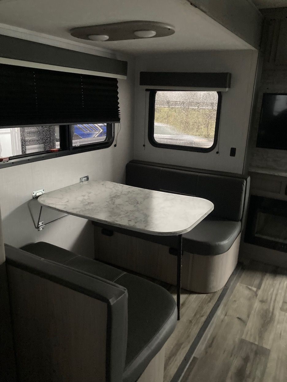 Interior RV dining area: Table with seating, window with blind, fireplace, and wood-look flooring.