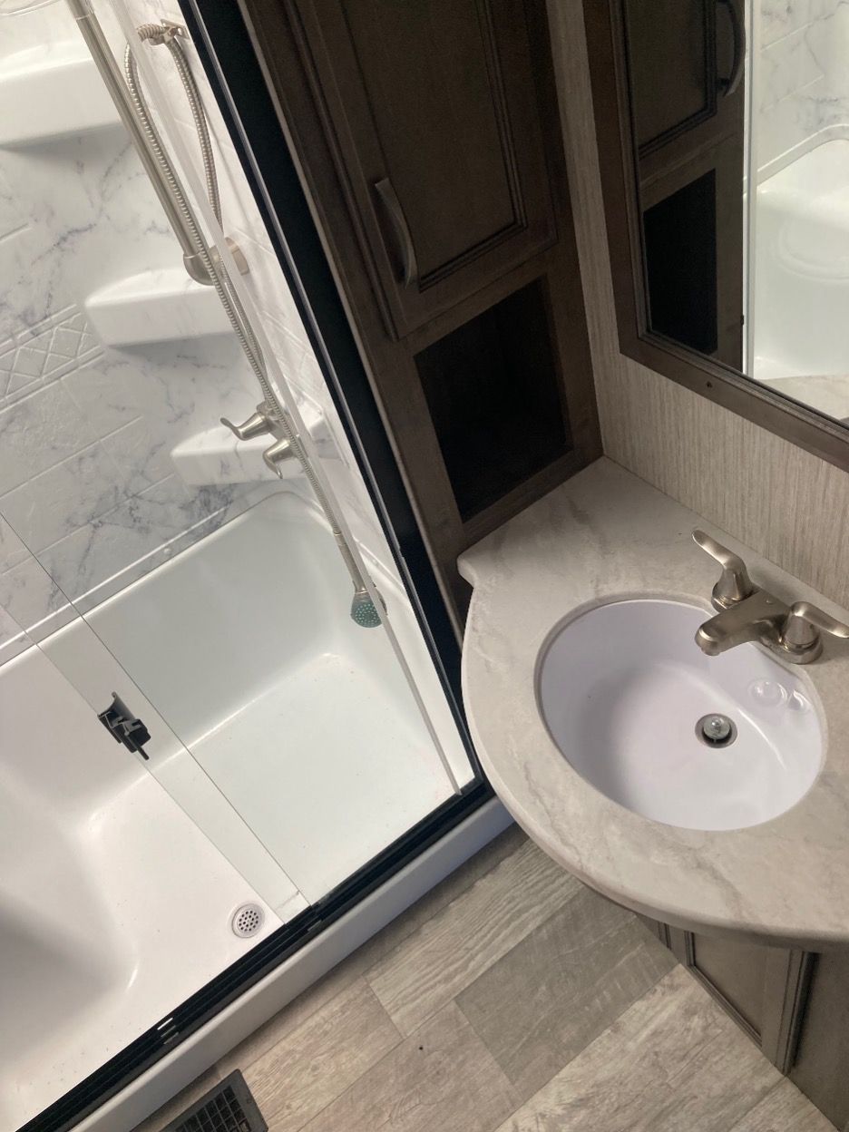 Bathroom in a recreational vehicle: shower with glass door, sink, and cabinet.