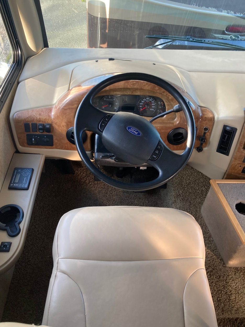 Interior of RV cab: steering wheel, dashboard, driver's seat. Beige and wood-tone details.