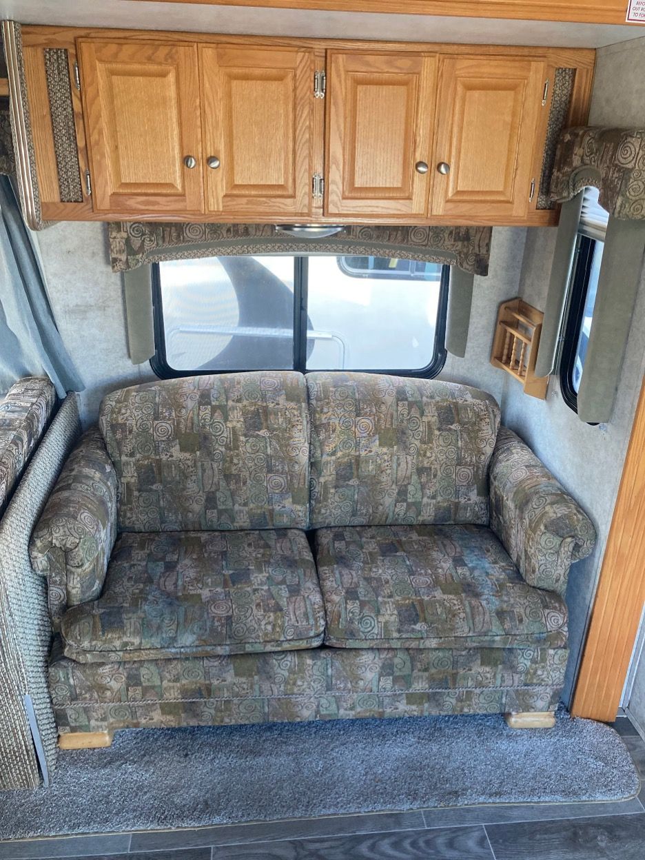 Tan floral couch below closed cabinets in a camper interior, with window and side mirror.