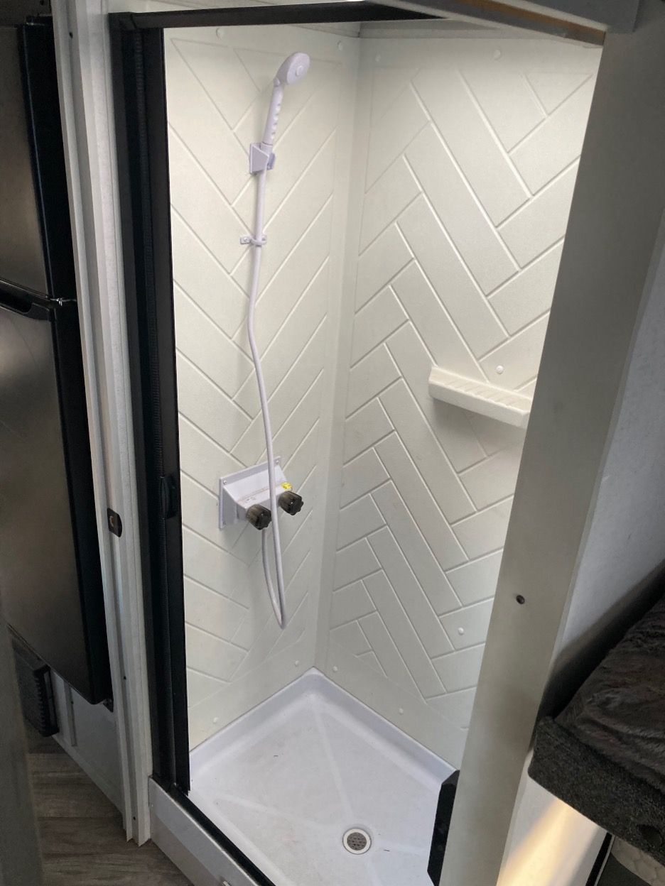 White tiled shower stall with a handheld shower head in a small bathroom.