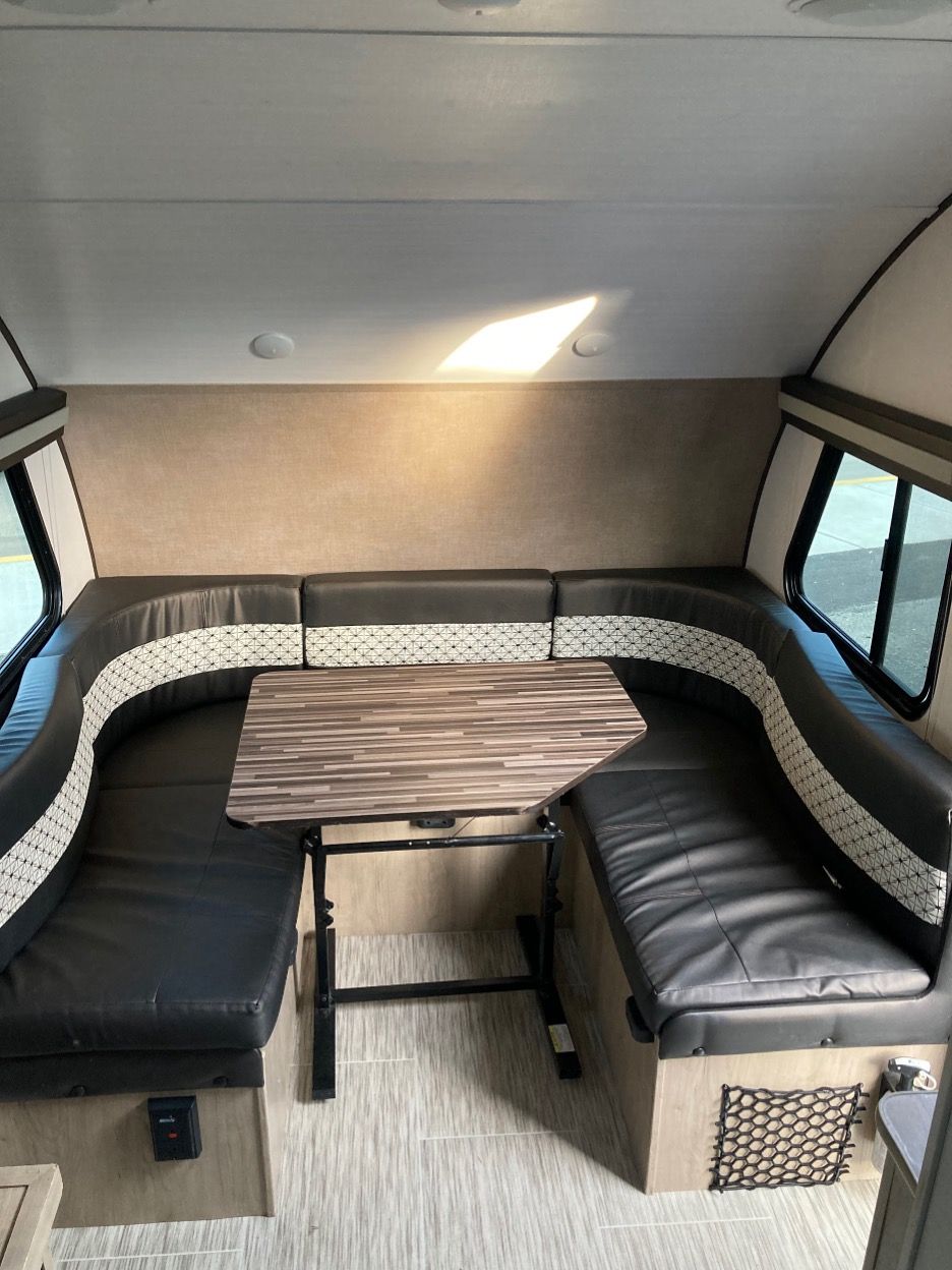 Interior of a camper with a U-shaped seating area, small table, and windows.
